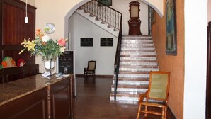 A reception area with a counter, a vase of flowers, a clock, and a staircase leading to an upper floor. - Hotel Posada Doña Lala (Tlacotalpan)