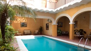 A swimming pool with a tiled deck, surrounded by potted plants and outdoor furniture. - Hotel Posada Doña Lala (Tlacotalpan)