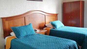 A room with two beds, a wooden headboard, a nightstand, a wardrobe, and a painting on the wall.