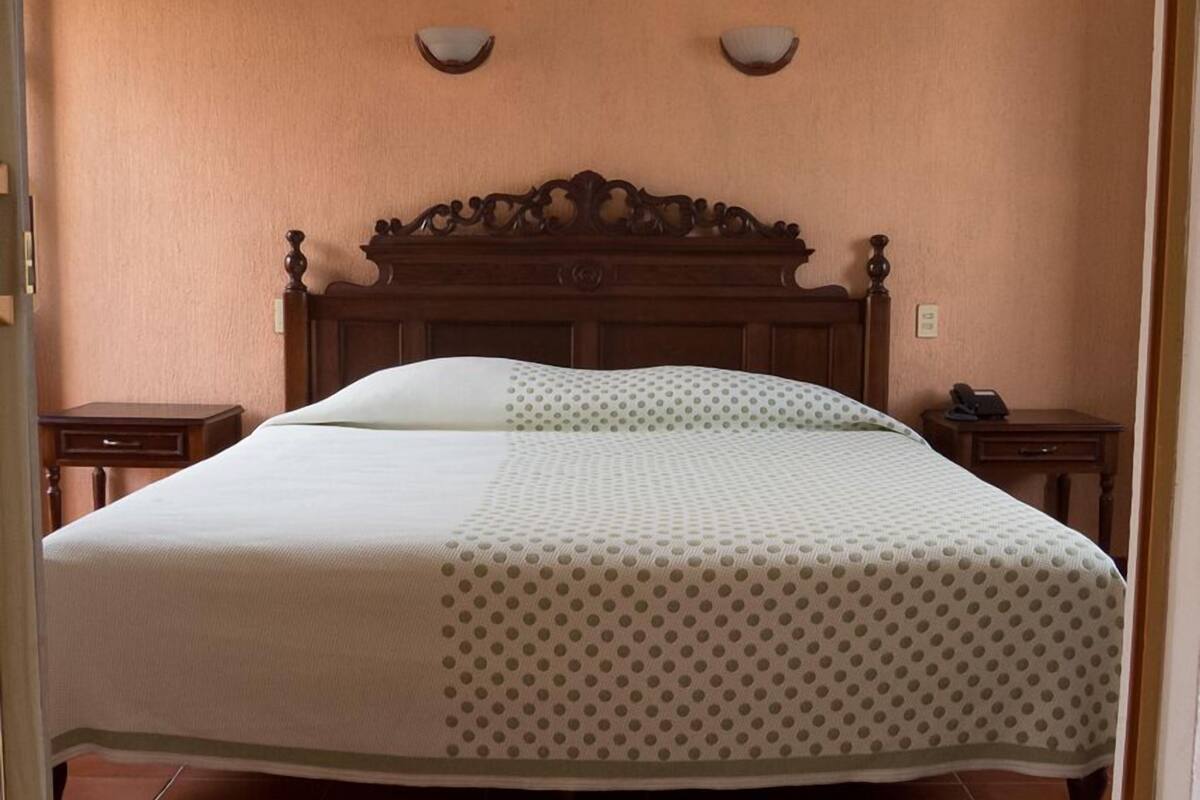 A neatly made bed with a polka dot bedspread, a wooden headboard, and two bedside tables with lamps.