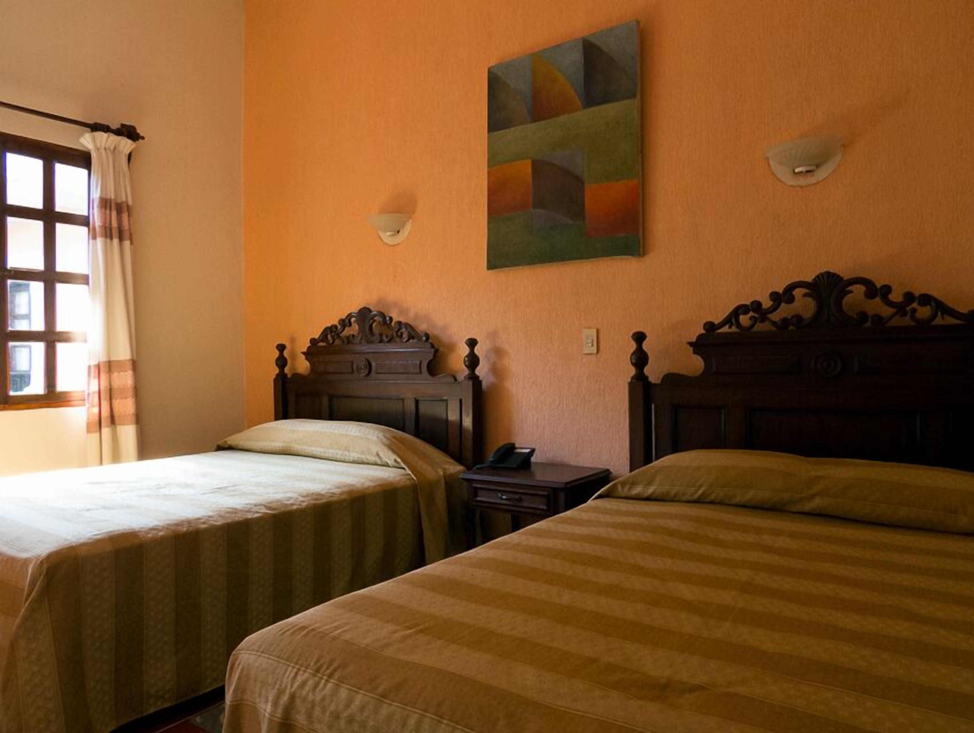 Two single beds with wooden headboards, a window with curtains, and a painting on the wall.