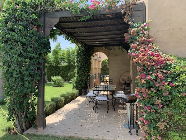 An outdoor patio with a pergola, a table and chairs, and a brick oven.