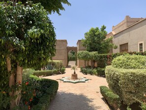 A courtyard with a central fountain, surrounded by neatly trimmed hedges and trees.