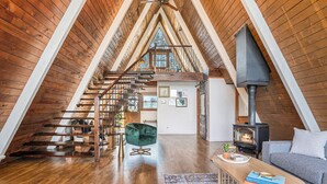 A spacious attic room with wooden beams, a staircase, a fireplace, and a cozy seating area. - Lakefront A-Frame: Private Beach, Fire Pit, Kayaks, Paddleboards, & Boat Slip (Decatur)