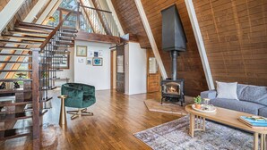 A spacious loft with a wooden staircase, a cozy seating area, and a wood-burning stove. - Lakefront A-Frame: Private Beach, Fire Pit, Kayaks, Paddleboards, & Boat Slip (Decatur)