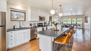 A modern kitchen with white cabinetry, a central island, bar stools, and pendant lighting. - Lakefront A-Frame: Private Beach, Fire Pit, Kayaks, Paddleboards, & Boat Slip (Decatur)