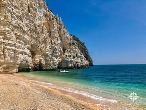 A coastal scene with a rocky cliff, clear turquoise waters, and a pebble beach. - Infinito - Attico sul Mare (Vieste)