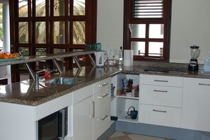 A kitchen with granite countertops, a sink, a blender, and a window with blinds. - Beautiful villa on Blue Bay (Sint Michiel)