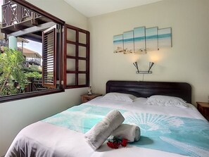A hotel room with a bed, a window with a view of greenery, and a wall with a painting. - Beautiful villa on Blue Bay (Sint Michiel)