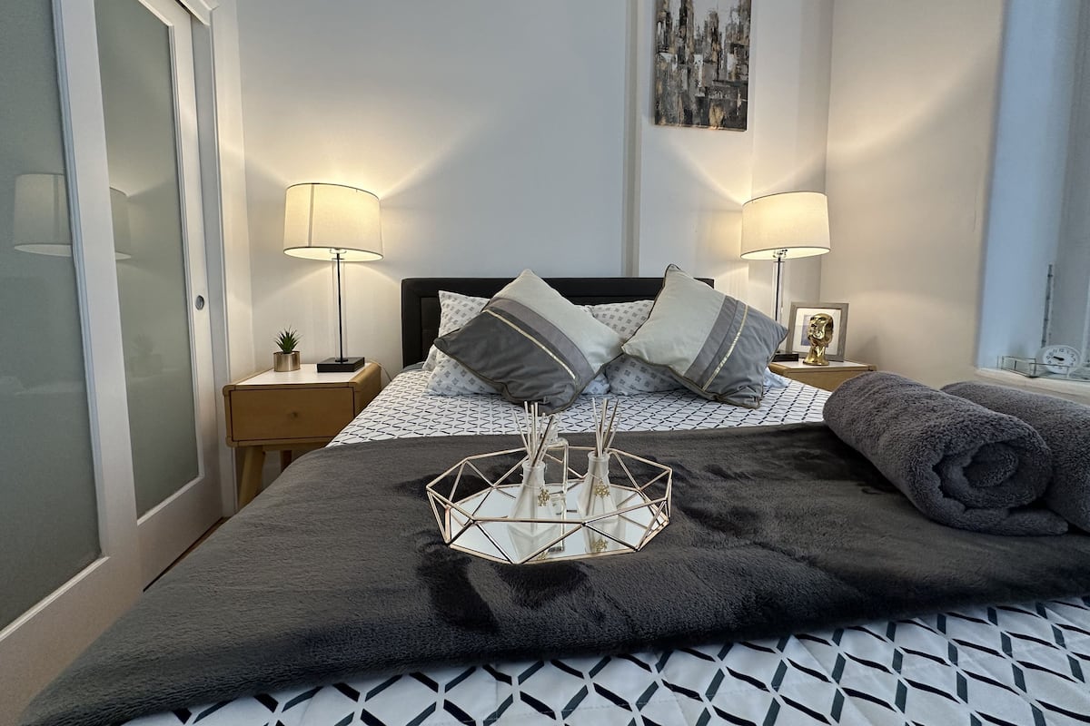 Une chambre à coucher bien rangée, avec un lit, deux tables de chevet, une horloge murale et un tableau encadré.