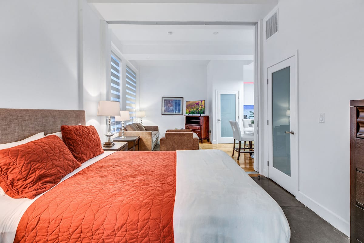 Une chambre d’hôtel avec un grand lit, un bureau avec une chaise, une petite table et une porte donnant sur un balcon.