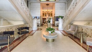 A grand lobby with a central round table, two sofas, and a staircase.