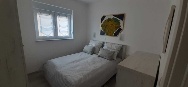 A bedroom with a bed, pillows, a window, and a painting on the wall. - 3 Zimmer Wohnung Neubau 100 Meter zum Strand (Rab)