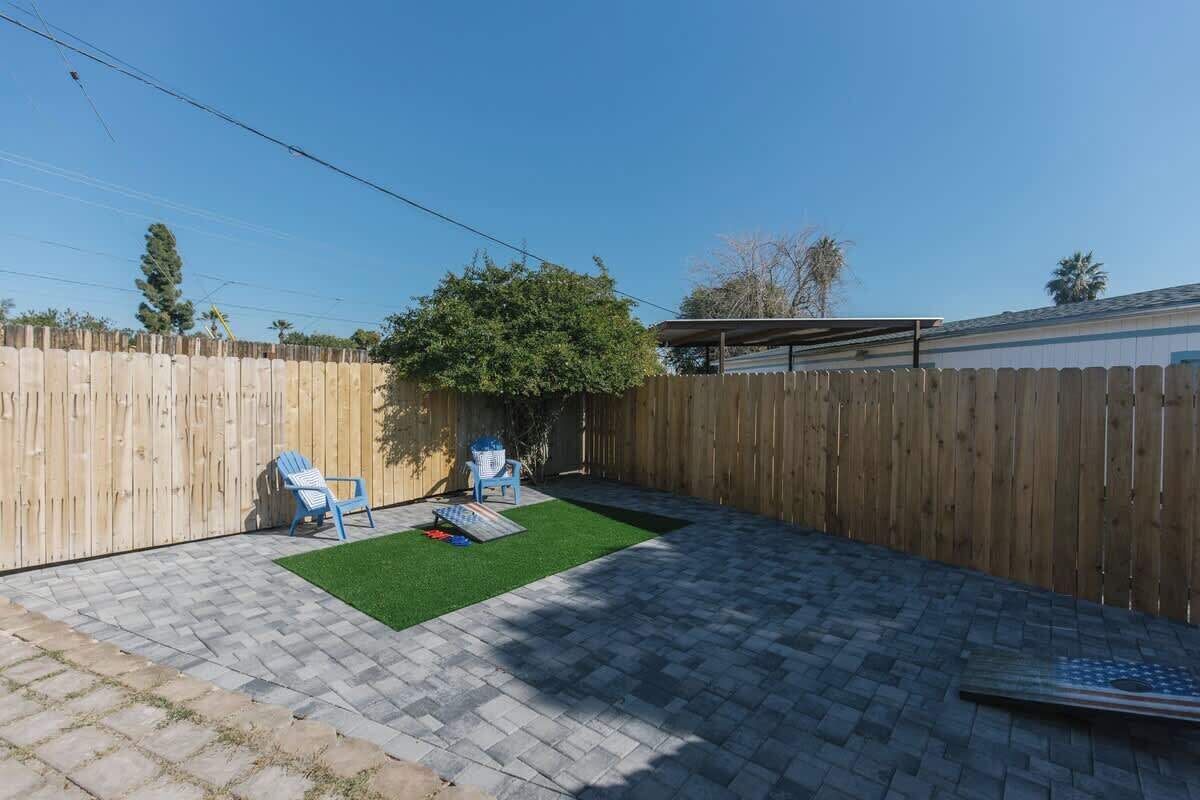 Un jardin avec une clôture en bois, deux chaises bleues, un arbre et une petite portion de gazon artificiel.