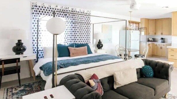 Ein modernes Schlafzimmer mit Bett, Nachttisch, Lampe und Blick auf die Küche.
