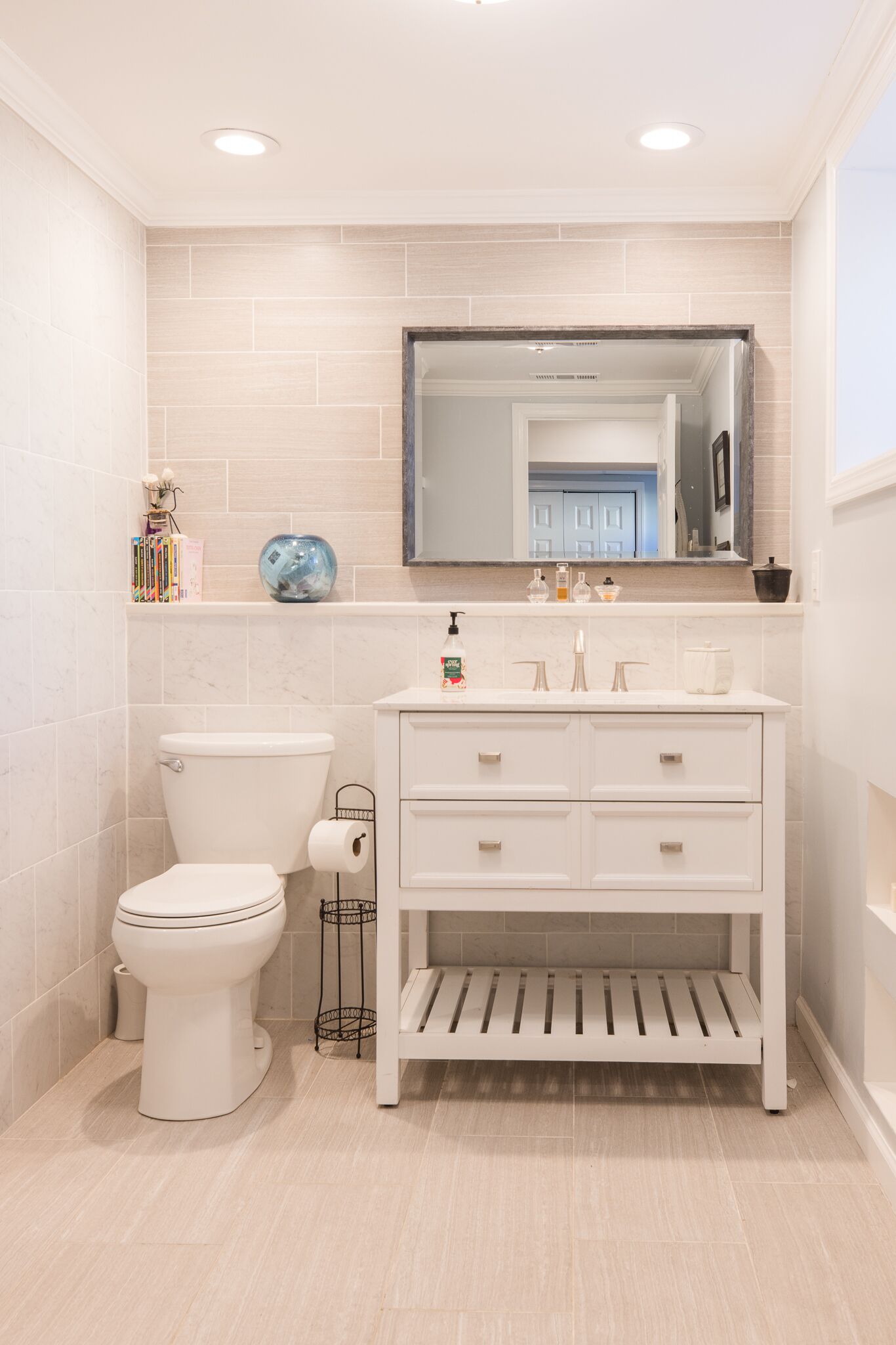 A bathroom with a toilet, a sink with a mirror above, and a shelf with toiletries.