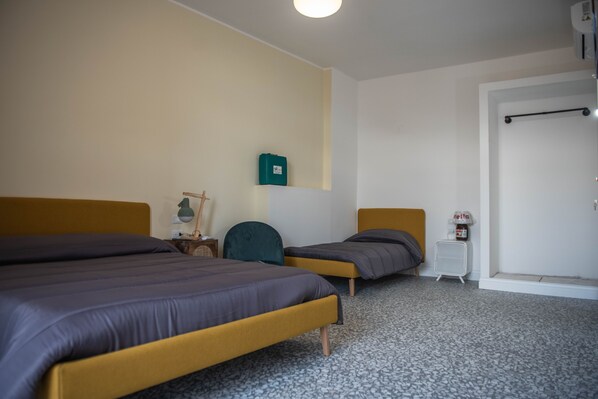 A hotel room with two beds, a small bedside table, a lamp, and a green trash bin.