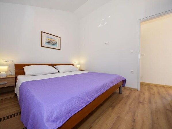 Un dormitorio con cama de madera, almohadas blancas, colcha morada y un cuadro en la pared.