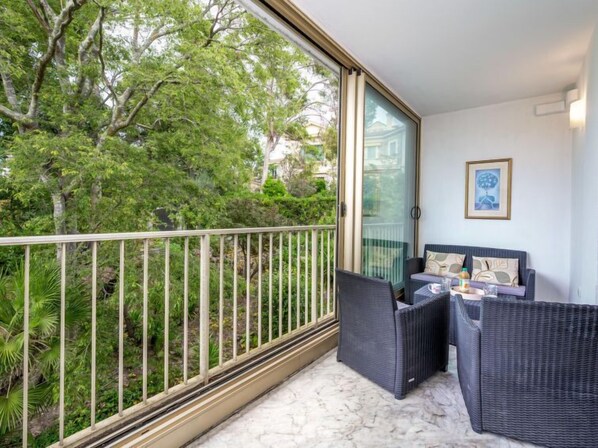 A balcony with wicker furniture, a glass door, and a view of greenery. - Val Joli by Interhome (Cannes)
