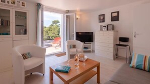 Un salon moderne comprenant un canapé, des fauteuils, une table basse, un téléviseur et un balcon avec vue sur les arbres.