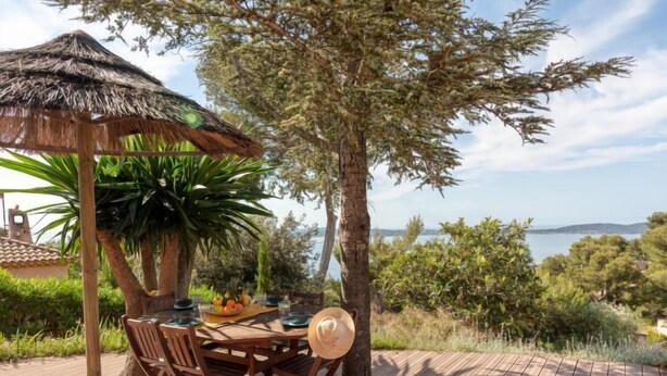 Un espace de restauration en plein air avec une table et des chaises en bois, un parasol en chaume et une vue sur la mer.