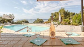 Un espace aménagé au bord de la piscine, avec vue sur la mer, une bouteille de vin et deux verres à vin vides sur une table carrelée.