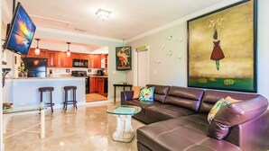 A modern living room with a brown leather sofa, a glass coffee table, and a TV mounted on the wall. - Zen Beach Villa w/ Pool & Garden Views, BBQ (Naples)
