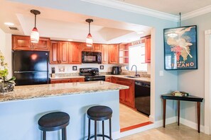 Prepare meals and socialize at the central island with two barstools, featuring a stainless steel refrigerator, microwave, and dishwasher.