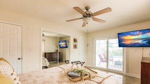 A bedroom with a bed, a ceiling fan, a TV, and a large window. - Zen Beach Villa w/ Pool & Garden Views, BBQ (Naples)