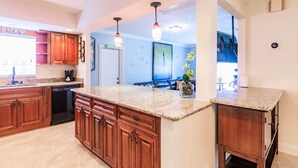 A modern kitchen with granite countertops, wooden cabinets, and pendant lighting. - Zen Beach Villa w/ Pool & Garden Views, BBQ (Naples)