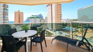 Un balcone con tavolo e sedie, ringhiera in vetro e vista su edifici e una montagna.