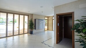 Un'ampia hall con pavimento piastrellato, una pianta in vaso, un display a parete e una porta dell'ascensore in legno.