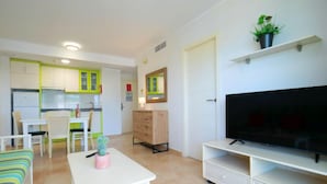 Una sala de estar moderna con televisor de pantalla plana, un comedor con mesa y sillas, y una cocina con armarios verdes.