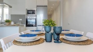 Eine moderne Küche mit Edelstahlgeräten, einem Esstisch mit blauen Tellern und Vasen sowie Blick in den angrenzenden Wohnbereich.