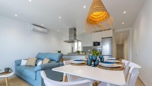 Ein modernes Wohnzimmer mit einem blauen Sofa, einem Esstisch mit weißen Stühlen und einer Küche im Hintergrund.