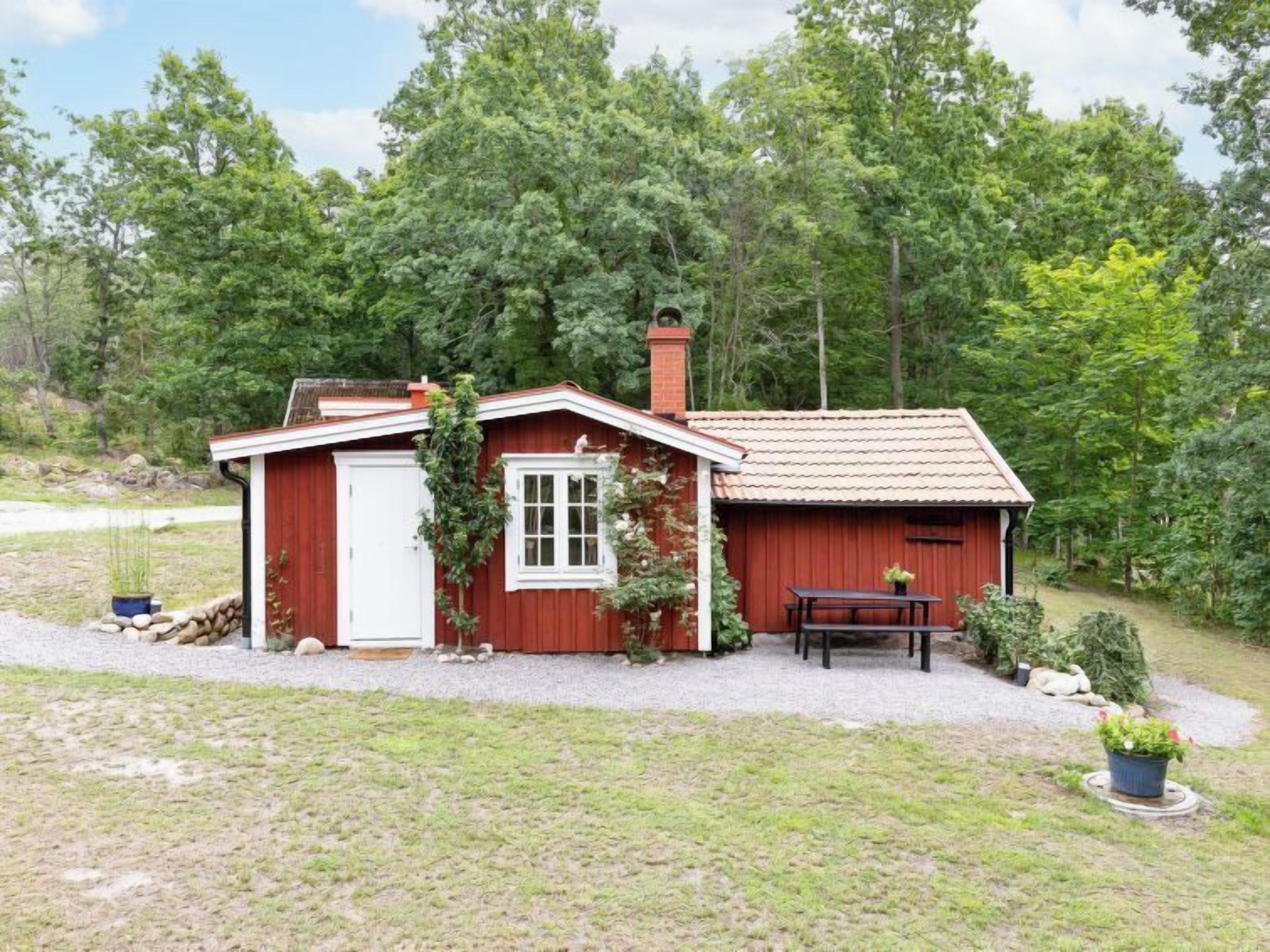 Ein kleines, rotes Holzhaus mit weißer Tür und Fenstern, umgeben von einer Schotterauffahrt und einem Rasen.