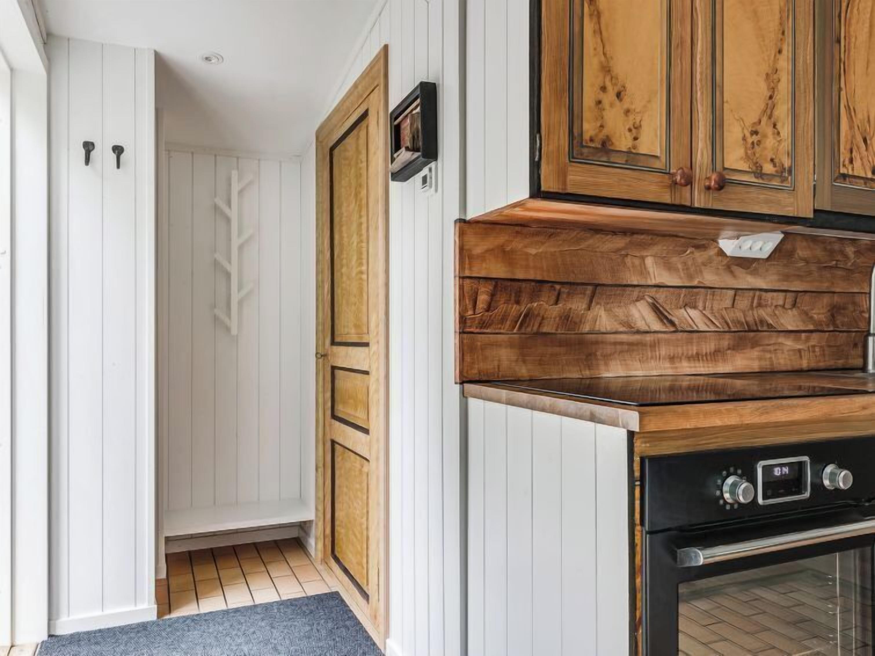A kitchen with white paneling, a wooden cabinet, and a black oven.