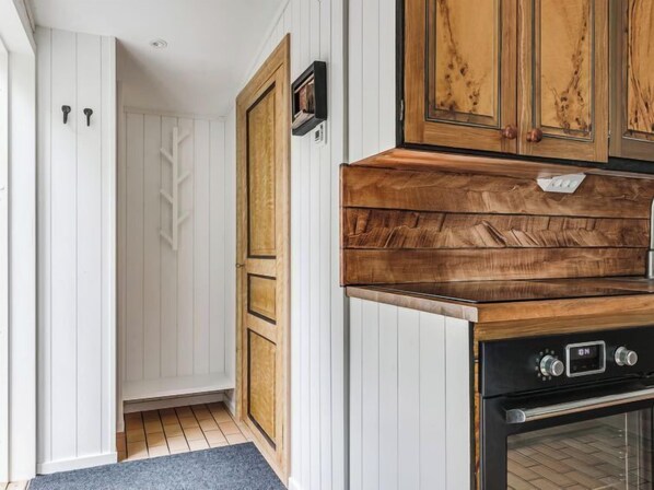A kitchen with white paneling, a wooden cabinet, and a black oven. - Vacation home Jennys by Interhome (Jämjö)