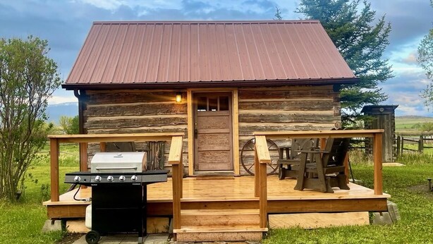 Ein rustikales Holzhaus mit Metalldach, einer Holzveranda und einem Steinweg, der zu einem Grill führt.