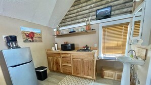 Eine kleine Küche mit Holdekor, einer integrierten Mikrowelle, einem Kühlschrank, einer Spüle und einem Fenster mit Jalousien.