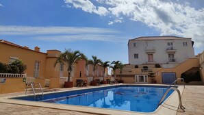 A swimming pool with a tiled deck, surrounded by buildings with balconies and palm trees. - Arenitas Beach.  An oasis by the sea (CN)