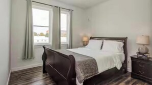 A bedroom with a bed, a nightstand, a window with curtains, and a view of the outside.