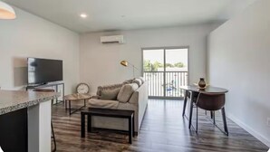 A modern living room with a flat-screen TV, a sofa, a coffee table, and a dining area with a small table and chairs.