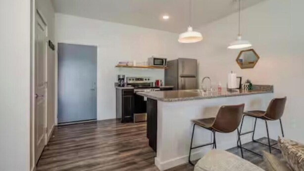 A modern kitchen with a central island, bar stools, a microwave, and a refrigerator.