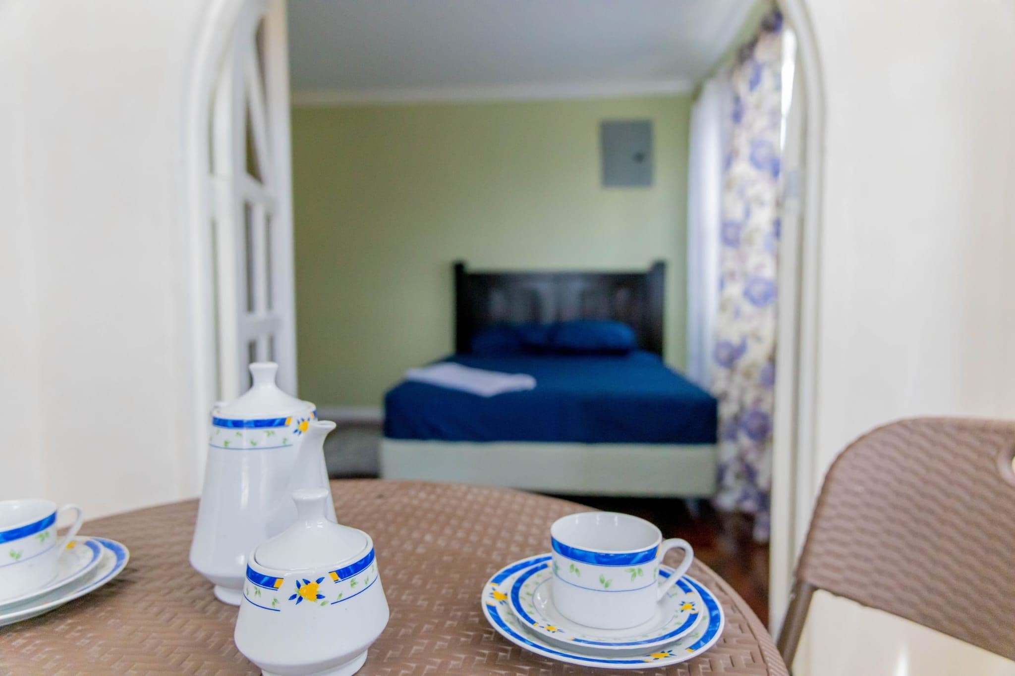 A room with a bed, a table with a teapot, cups, and saucers.
