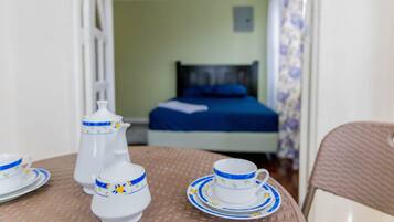 A room with a bed, a table with a teapot, cups, and saucers.