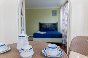 A room with a bed, a table with a teapot, cups, and saucers.