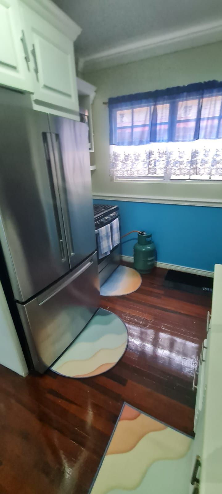 A kitchen with a refrigerator, stove, and gas cylinder.