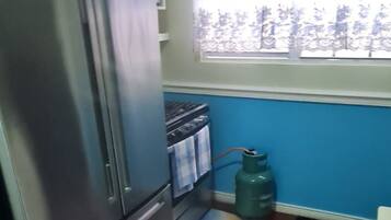 A kitchen with a refrigerator, stove, and gas cylinder.