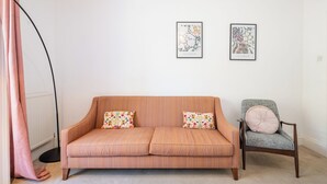 Ein Zimmer mit einer Couch und einem Sessel, zwei gerahmte Kunstwerke an der Wand und einer Stehlampe.